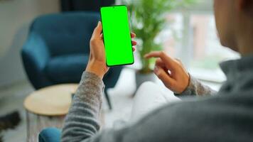 Frau beim Zuhause mit Smartphone mit Grün Attrappe, Lehrmodell, Simulation Bildschirm im Vertikale Modus. Mädchen Surfen Internet, Aufpassen Inhalt video