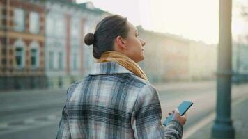 femme dans une manteau permanent sur le rue dans le de bonne heure Matin et en utilisant téléphone intelligent video