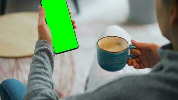 Frau beim Zuhause mit Smartphone mit Grün Attrappe, Lehrmodell, Simulation Bildschirm im Vertikale Modus und Trinken Kaffee video