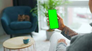 mujer a hogar utilizando teléfono inteligente con verde Bosquejo pantalla en vertical modo. niña hojeada Internet, acecho contenido video