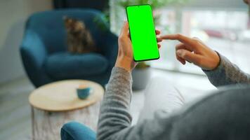 mujer a hogar utilizando teléfono inteligente con verde Bosquejo pantalla en vertical modo. niña hojeada Internet, acecho contenido video