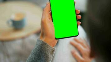 Woman at home using smartphone with green mock-up screen in vertical mode. Girl browsing Internet, watching content video