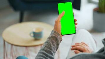 vrouw Bij huis gebruik makend van smartphone met groen mock-up scherm in verticaal modus. meisje browsen internetten, aan het kijken inhoud video