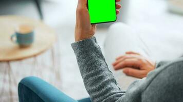 Woman at home using smartphone with green mock-up screen in vertical mode. Girl browsing Internet, watching content video