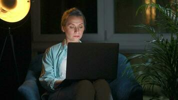 Woman is sitting in the armchair and makes an online purchase using a credit card and laptop at night video