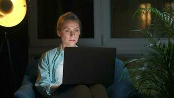 Woman is sitting in the armchair and makes an online purchase using a credit card and laptop at night video