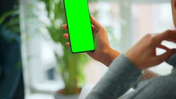 Woman at home using smartphone with green mock-up screen in vertical mode. Girl browsing Internet, watching content video