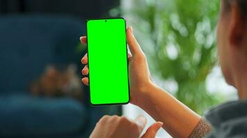 femme à Accueil en utilisant téléphone intelligent avec vert maquette écran dans verticale mode. fille navigation l'Internet, en train de regarder contenu video