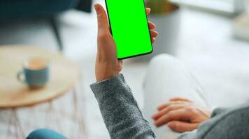 mujer a hogar utilizando teléfono inteligente con verde Bosquejo pantalla en vertical modo. niña hojeada Internet, acecho contenido video