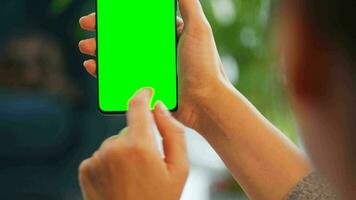 Woman at home using smartphone with green mock-up screen in vertical mode. Girl browsing Internet, watching content video