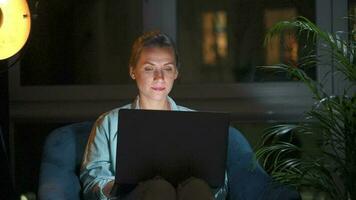 donna è seduta nel il poltrona e fa un in linea Acquista utilizzando un' credito carta e il computer portatile a notte video