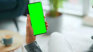 Woman at home using smartphone with green mock-up screen in vertical mode. Girl browsing Internet, watching content video