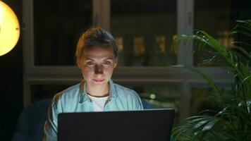 Woman is sitting in the armchair and working on a laptop at night. Concept of remote work video