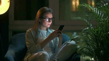 mujer es sentado en el Sillón y hace un en línea compra utilizando un crédito tarjeta y teléfono inteligente a noche video