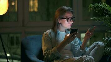 mujer es sentado en el Sillón y hace un en línea compra utilizando un crédito tarjeta y teléfono inteligente a noche video