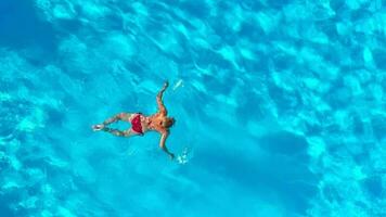 Aerial view of a woman in red swimsuit swimming in the pool. Summer lifestyle video