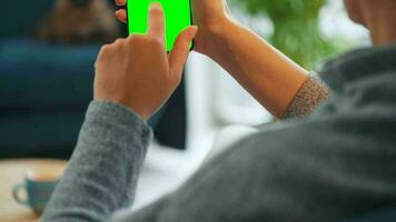 Woman at home using smartphone with green mock-up screen in vertical mode. Girl browsing Internet, watching content video