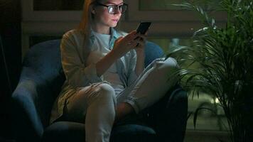 Woman is sitting in the armchair and makes an online purchase using a credit card and smartphone at night video