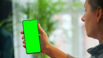 Woman at home using smartphone with green mock-up screen in vertical mode. Girl browsing Internet, watching content video