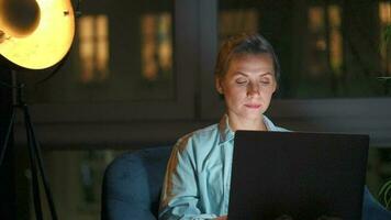 Woman is sitting in the armchair and makes an online purchase using a credit card and laptop at night video