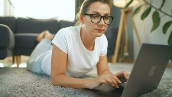 Woman with glasses is lying on the floor and working on a laptop. Concept of remote work video