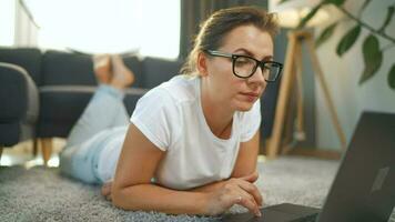 mujer con lentes es acostado en el piso y trabajando en un ordenador portátil. concepto de remoto trabajo video