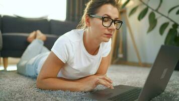 Woman with glasses is lying on the floor and working on a laptop. Concept of remote work video