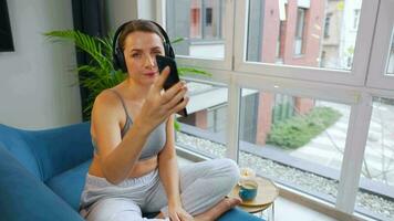 gelukkig ontspannen vrouw in draadloze hoofdtelefoons luisteren naar muziek- en gebruik makend van mobiel apps of communiceert Aan sociaal netwerken Aan smartphone video