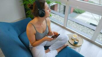 Happy relaxed woman in wireless headphones listening to music and using mobile apps or communicates on social networks on smartphone video