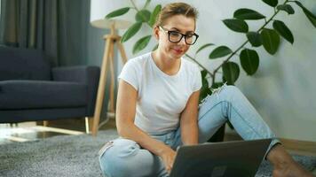 ritratto di un' donna con bicchieri guardare a il telecamera al di sopra di un' il computer portatile nel il interno di un' accogliente appartamento. concetto di moderno stile di vita e a distanza opera video