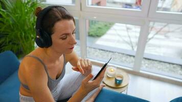 Happy relaxed woman in wireless headphones listening to music and using mobile apps or communicates on social networks on smartphone video