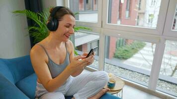 content détendu femme dans sans fil écouteurs écoute à la musique et en utilisant mobile applications ou communique sur social réseaux sur téléphone intelligent video