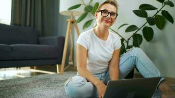 portrait de une femme avec des lunettes à la recherche à le caméra plus de une portable dans le intérieur de une confortable appartement. concept de moderne mode de vie et éloigné travail video