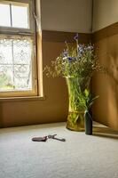 Bunch of autumn flowers in a vase on the window and keys of the home of the table in the corner of the room. Vertical view photo