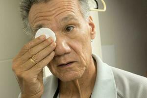 Senior man in the bathroom using cotton pads for eye relief photo