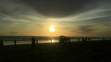 hermosa puesta de sol con el mar en el antecedentes. el Dom más allá el horizonte ilumina el Oceano y nubes en el cielo. allí son personas y carruajes alrededor. video