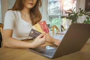 cierre la mano femenina sosteniendo la tarjeta de crédito y eligiendo usar. mujer joven que usa computadora portátil para banca digital, pago por Internet, compras en línea, tecnología financiera, concepto de comercio electrónico. foto