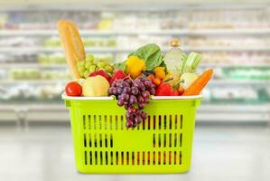 Shopping basket with fruits and vegetables in supermarket grocery store blurred background photo