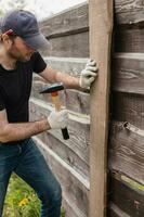 un adulto hombre es comprometido en carpintería trabajo a un casa construcción sitio - un de madera cerca y terraza tableros foto