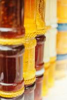 Glass jars with honey on the market - a variety of honey varieties in different shades and thicknesses photo