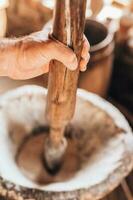 un hombre molinero panadero muele grano por mano en un de madera mortero utilizando antiguo tecnología foto