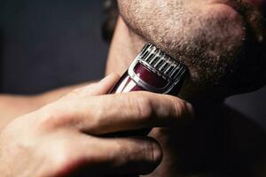 Attractive middle-aged man with well-groomed skin shaves his face with an electric razor after a shower - hygiene photo