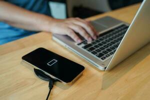 Charging mobile phone battery with wireless charging device in the table. Smartphone charging on a charging pad. Mobile phone near wireless charger Modern lifestyle technology concept photo