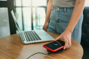 Charging mobile phone battery with wireless charging device in the table. Smartphone charging on a charging pad. Mobile phone near wireless charger Modern lifestyle concept. photo