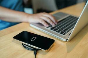 Charging mobile phone battery with wireless charging device in the table. Smartphone charging on a charging pad. Mobile phone near wireless charger Modern lifestyle technology concept photo