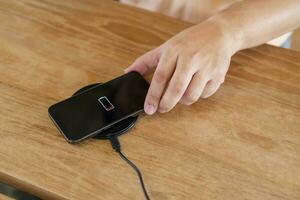 Charging mobile phone battery with wireless charging device in the table. Smartphone charging on a charging pad. Mobile phone near wireless charger Modern lifestyle technology concept. photo