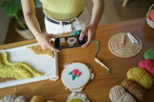 Asian Woman taking smartphone photo Punch needle. phone posting on social networks in studio workshop. designer workplace Handmade craft project DIY embroidery