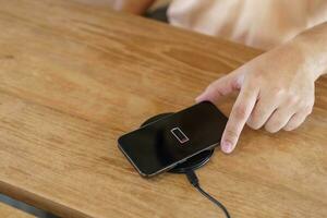 Charging mobile phone battery with wireless charging device in the table. Smartphone charging on a charging pad. Mobile phone near wireless charger Modern lifestyle technology concept. photo