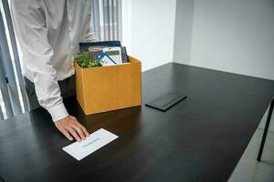 Business man sending resignation letter and packing Stuff Resign Depress or carrying business cardboard box by desk in office. Change of job or fired from company photo