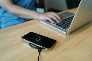 Charging mobile phone battery with wireless charging device in the table. Smartphone charging on a charging pad. Mobile phone near wireless charger Modern lifestyle technology concept photo